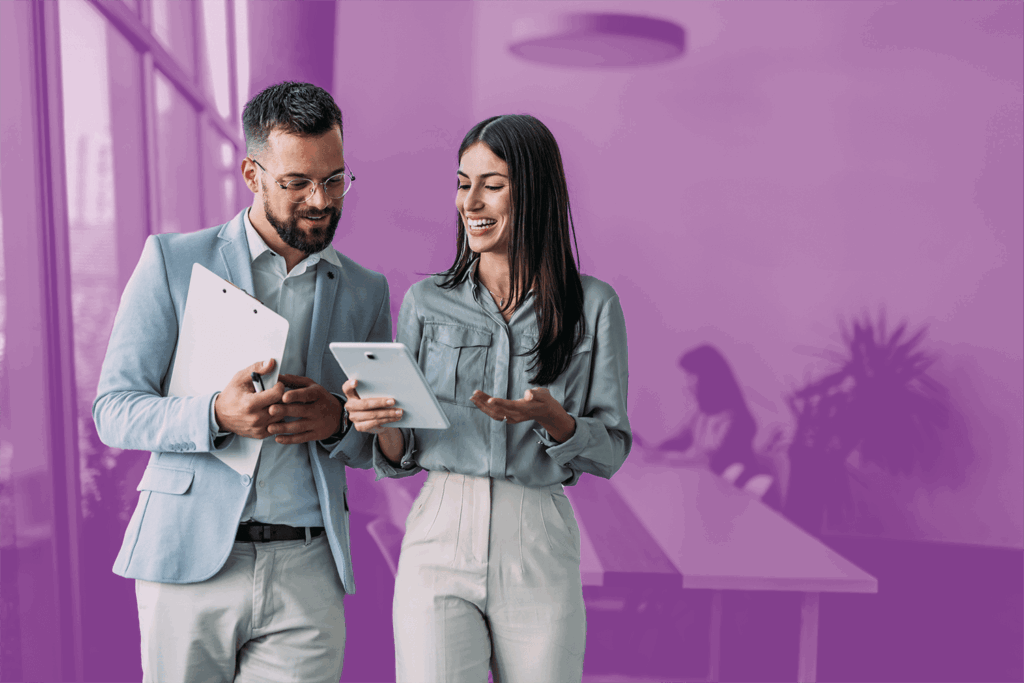 Two professionals smiling and discussing information on a tablet in a modern office setting.