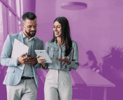 Two professionals smiling and discussing information on a tablet in a modern office setting.