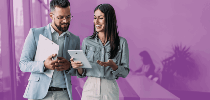 Two professionals smiling and discussing information on a tablet in a modern office setting.