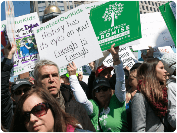 Crowd of protestors holding Sandy Hook Promise and gun reform signs during a public demonstration.
