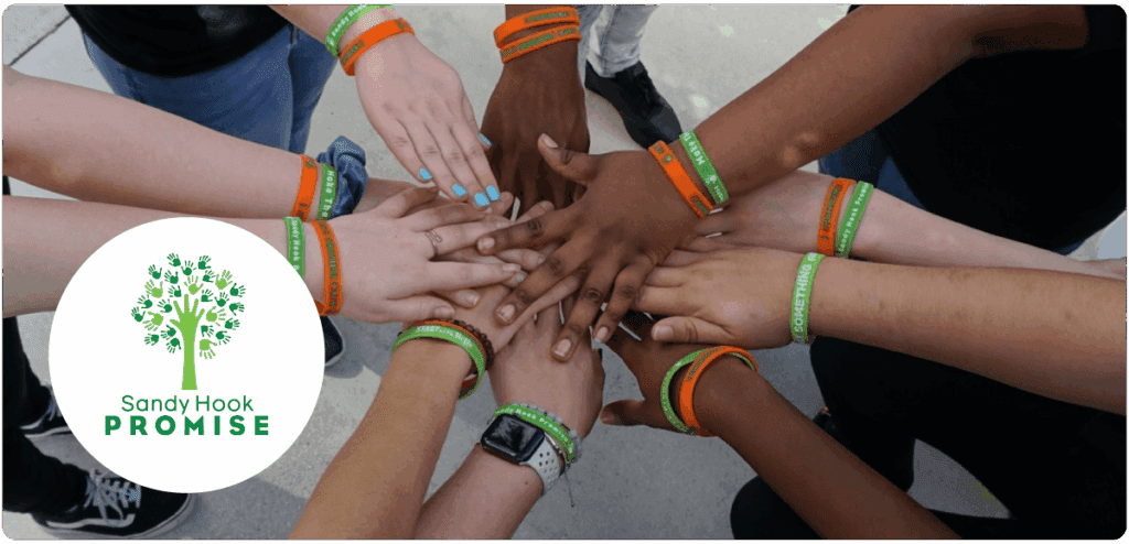 Diverse group of young people wearing Sandy Hook Promise wristbands with their hands stacked together in solidarity.