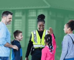 Smiling police officer gives a high five to a young girl while interacting with a family outdoors.