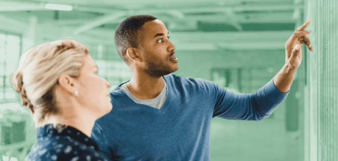 Man pointing at a board while discussing data with a colleague in a modern office.