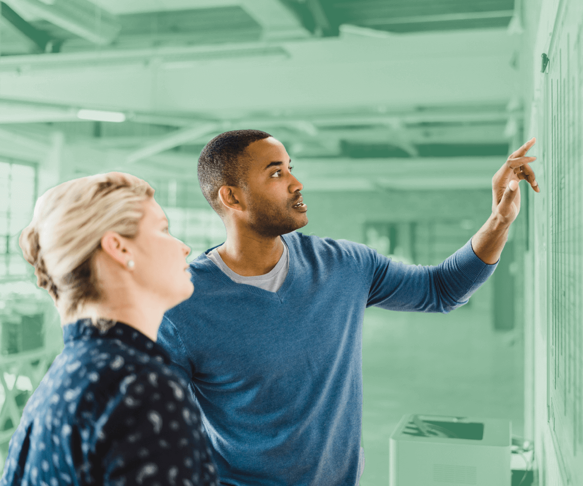 Man pointing at a board while discussing data with a colleague in a modern office.