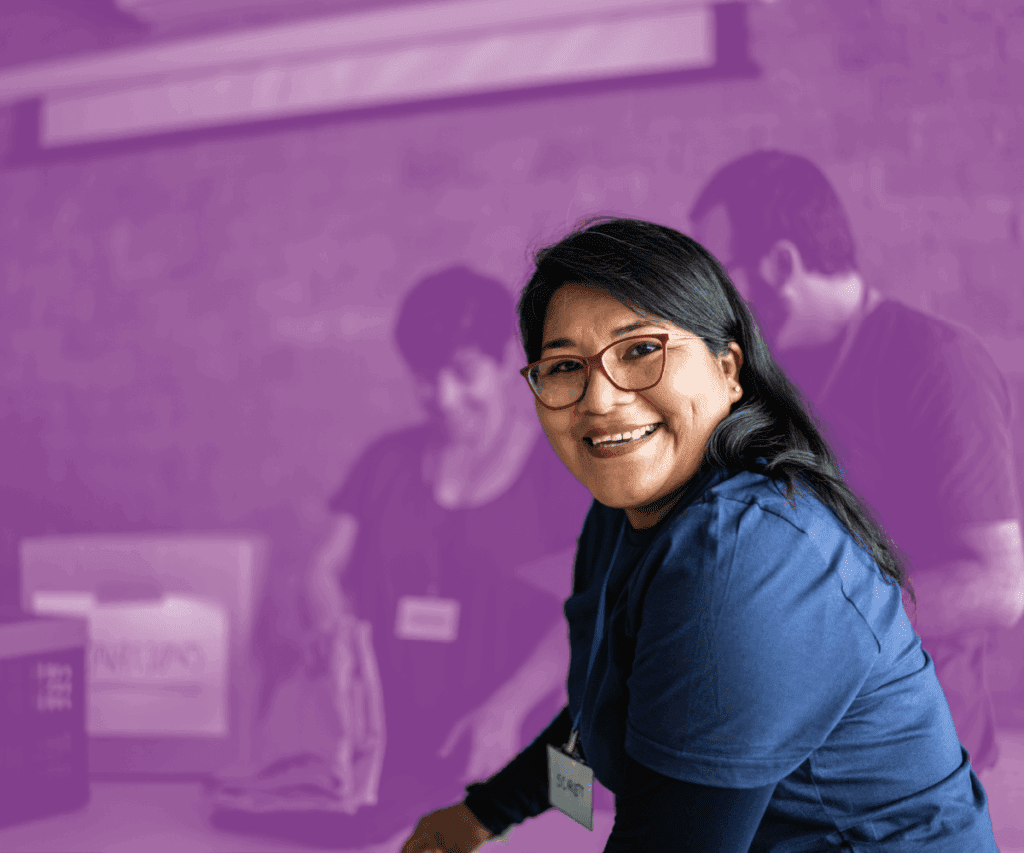 Smiling woman wearing a volunteer name tag in a community service setting with others working in the background.
