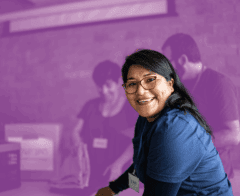 Smiling woman wearing a volunteer name tag in a community service setting with others working in the background.