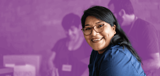 Smiling woman wearing a volunteer name tag in a community service setting with others working in the background.