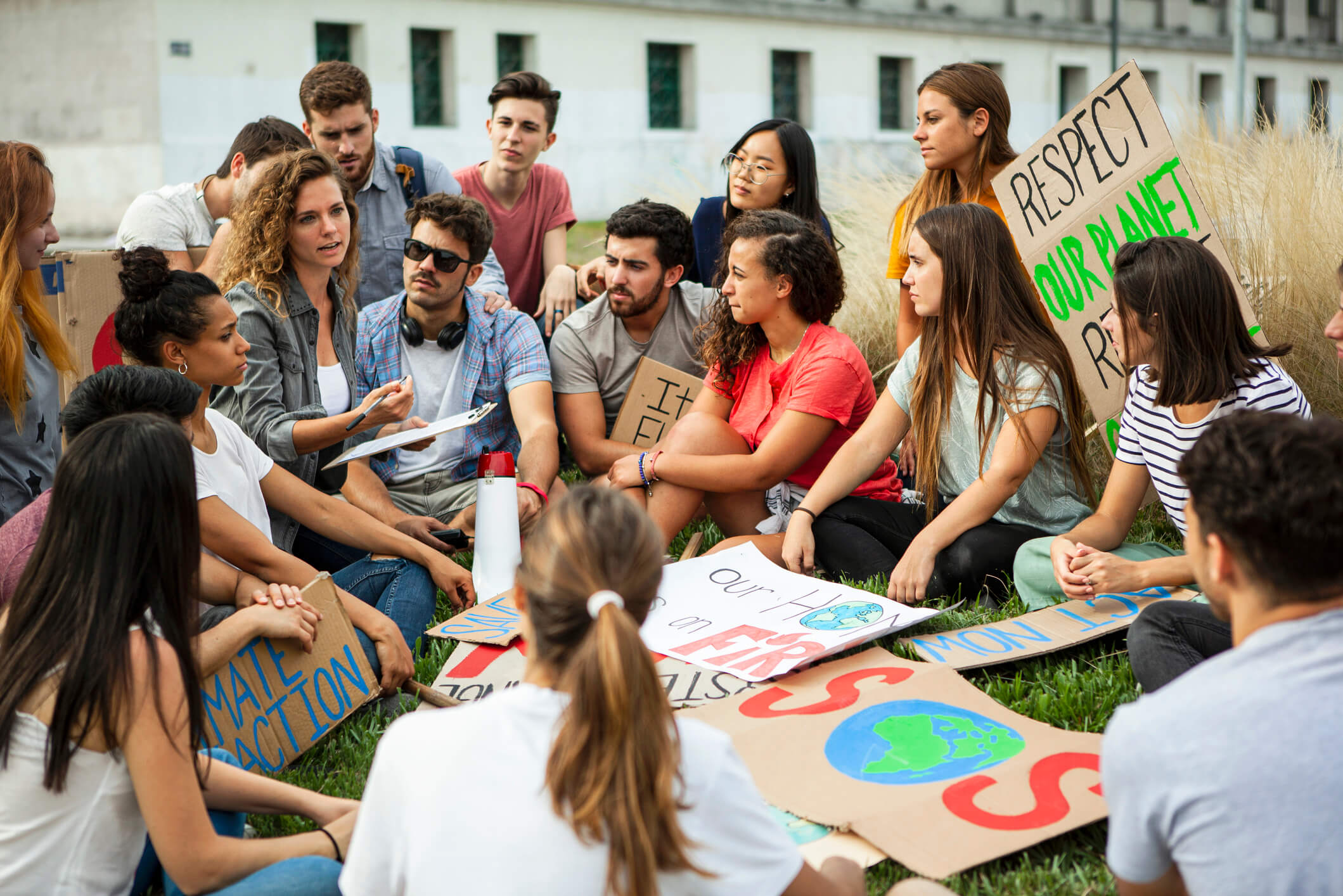 Group of young activists gathered outdoors holding climate protest signs and having a discussion.