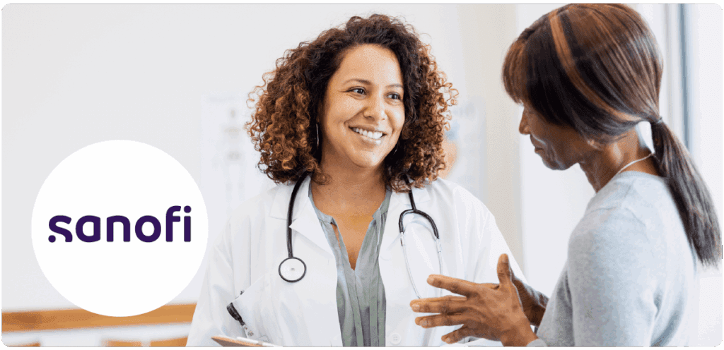 A smiling female doctor with curly hair wearing a white coat and stethoscope speaks with a patient. The Sanofi logo is displayed in a white circle on the left side of the image.