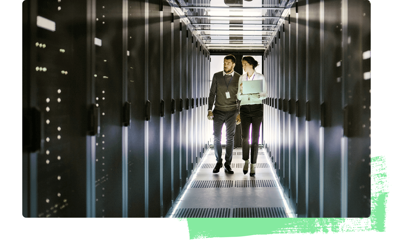 Two IT professionals walk down a brightly lit server room aisle lined with rows of black server racks. One holds a laptop as they talk, symbolizing data management, technology infrastructure, and environmental responsibility in AI operations.