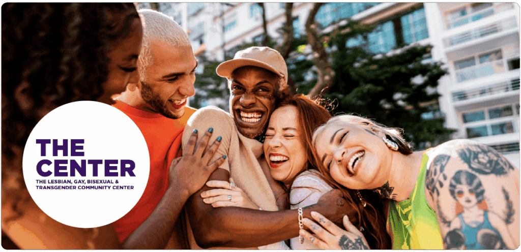 A group hug among friends outdoors in front of tall buildings. Everyone is smiling and laughing, conveying warmth and support. A white circle on the left displays the logo: “THE CENTER — The Lesbian, Gay, Bisexual & Transgender Community Center.”