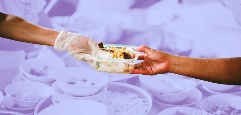 A gloved hand giving a container of food to another person, with purple-hued food behind them.