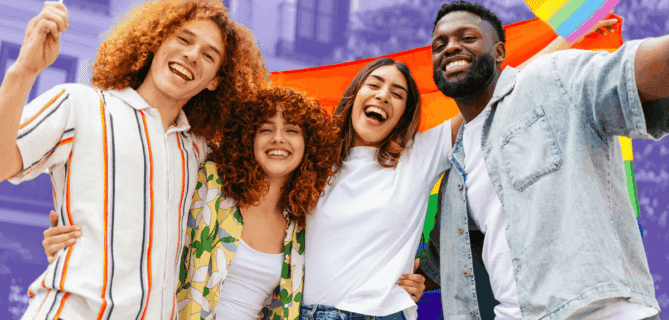 A diverse group of four friends stand together outdoors, smiling and holding rainbow Pride flags. They appear joyful and united, with a rainbow flag stretched behind them and buildings in the background.