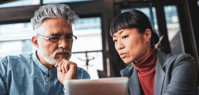 A man and woman sit together in a modern office, focusing intently on a tablet screen. The man rests his chin on his hand while the woman points or gestures toward the tablet, suggesting they are reviewing or discussing information related to AI or data analysis.