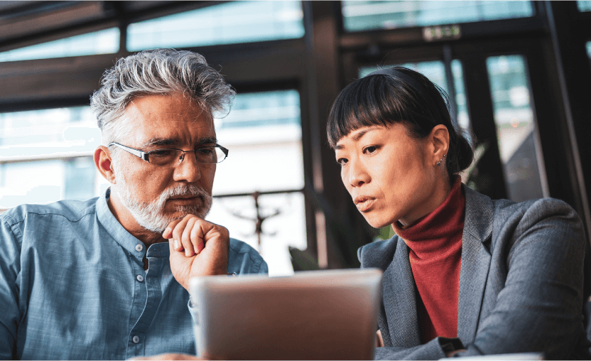 A man and woman sit together in a modern office, focusing intently on a tablet screen. The man rests his chin on his hand while the woman points or gestures toward the tablet, suggesting they are reviewing or discussing information related to AI or data analysis.