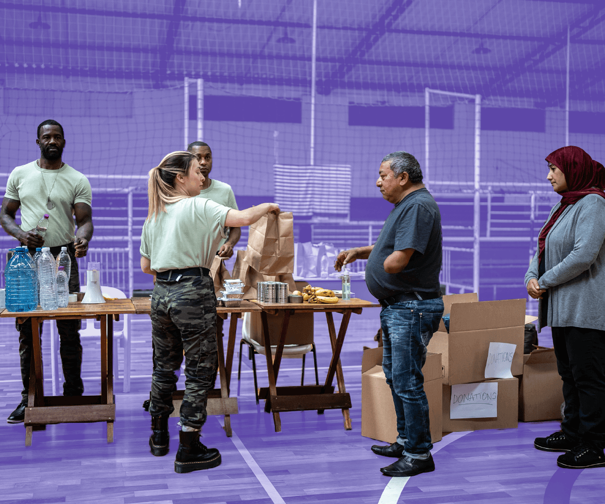 Volunteers distribute food and supplies to community members inside a gymnasium. People stand by donation boxes and tables with bottled water and packaged meals. The background is tinted purple to match Bonterra’s brand style.
