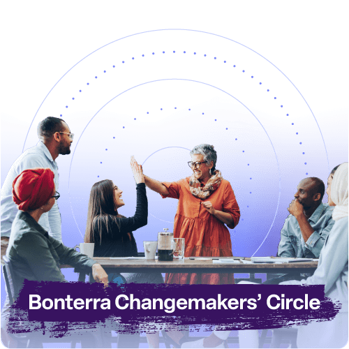 A diverse group of professionals sits around a table in discussion, smiling and engaged. One woman in a burnt-orange outfit high-fives a seated woman, symbolizing celebration and teamwork. The background features a soft purple gradient with circular graphic lines radiating outward, emphasizing connection and community. Text at the bottom reads “Bonterra Changemakers’ Circle.”