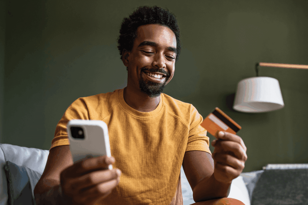 Smiling man holding a smartphone and credit card while making an online payment, representing seamless digital giving and donor convenience.