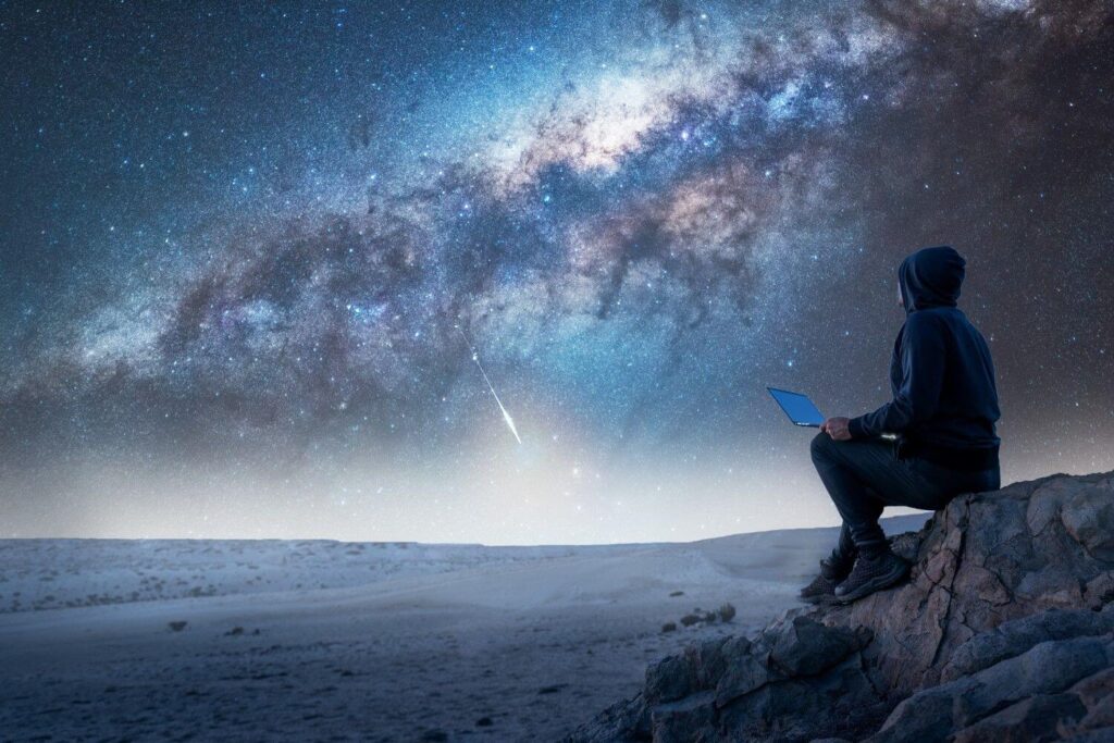 Person sitting on a rocky overlook at night using a laptop while gazing at the Milky Way, symbolizing strategic planning and clarity—representing the AI readiness matrix as a guiding framework for fundraising professionals navigating AI adoption.