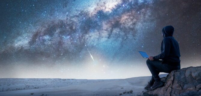 Person sitting on a rocky overlook at night using a laptop while gazing at the Milky Way, symbolizing strategic planning and clarity—representing the AI readiness matrix as a guiding framework for fundraising professionals navigating AI adoption.