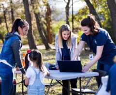 Volunteers gather around a table outdoors, using a laptop to coordinate activities during a community event.