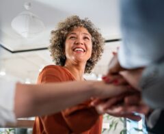 A smiling professional greets another person with a handshake in a bright, modern workspace.