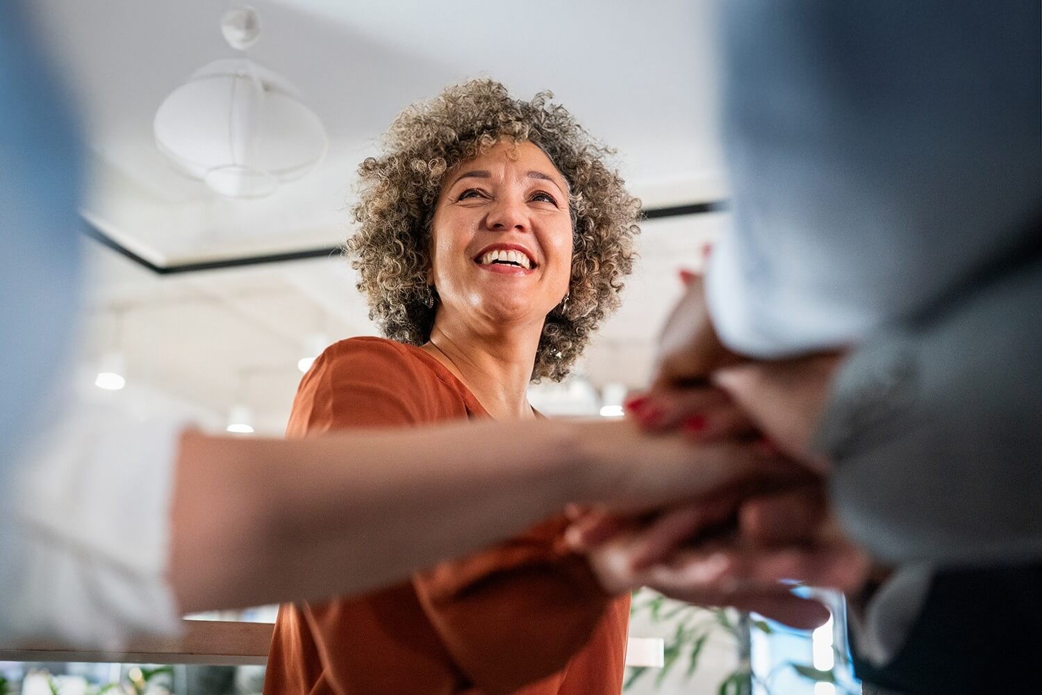 A smiling professional greets another person with a handshake in a bright, modern workspace.