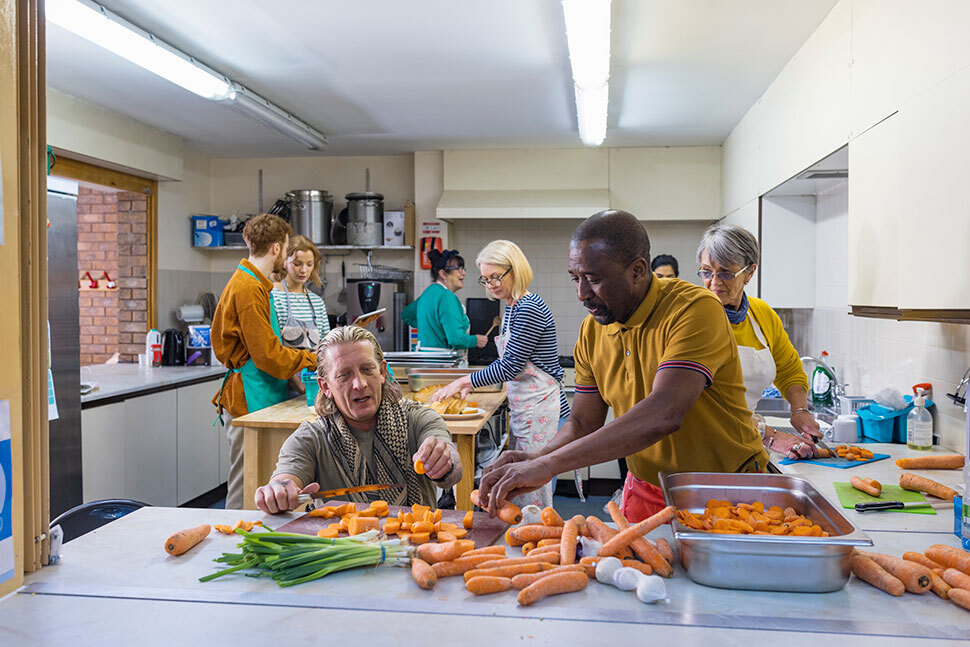 Community members and volunteers prepare food together in a shared kitchen as part of a public service or community support program.