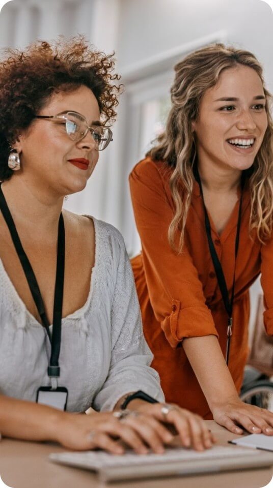 Two colleagues smile and collaborate while reviewing information together at a desk.