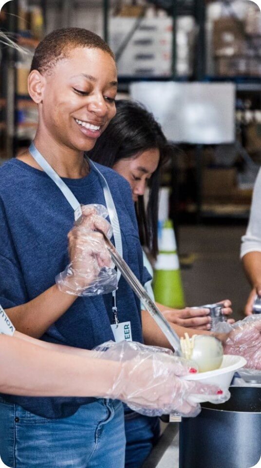A volunteer smiles while serving food during a community meal preparation activity.