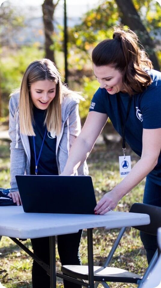 Two volunteers review information on a laptop at an outdoor event table.
