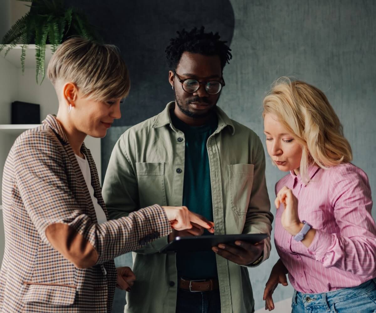 Three colleagues review information together on a tablet during a collaborative discussion.