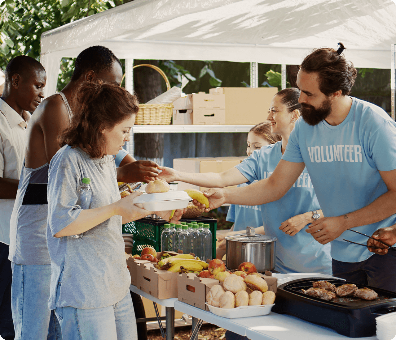 Volunteers distribute prepared meals and groceries to community members at an outdoor food service station.